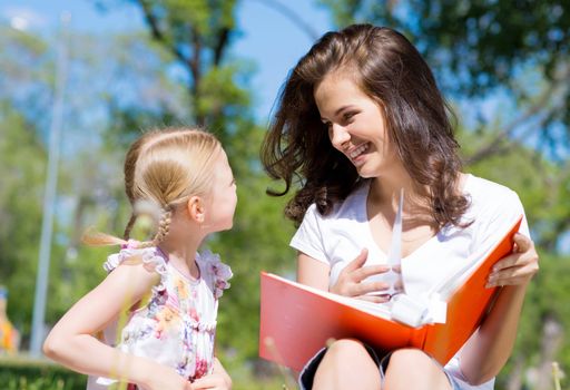 girl with the teacher reading a book together in the summer park