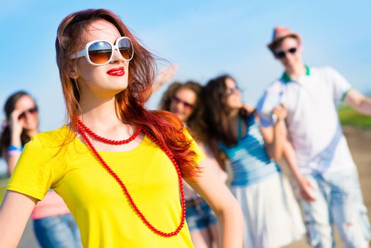 stylish young woman in sunglasses on the background of blue sky and friends