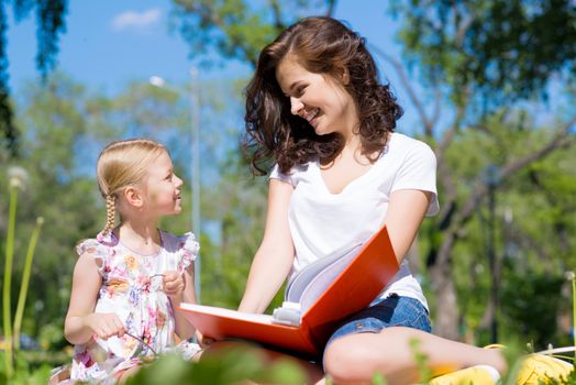 girl with the teacher reading a book together in the summer park