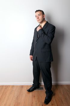 Business man adjusting his necktie standing in an empty room with wood floors.