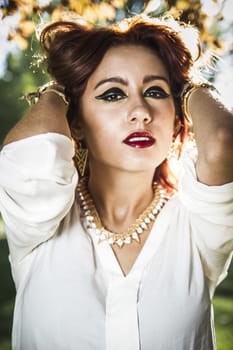 Beautiful young woman close-up in white sweater, against green of summer park.