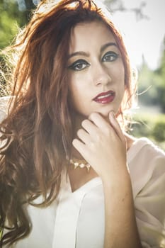 Portrait of pensive beautiful young woman, against background of summer green park.