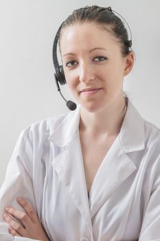 twenty something woman wearing a lab coat, a headset and great smile and , against a white wall