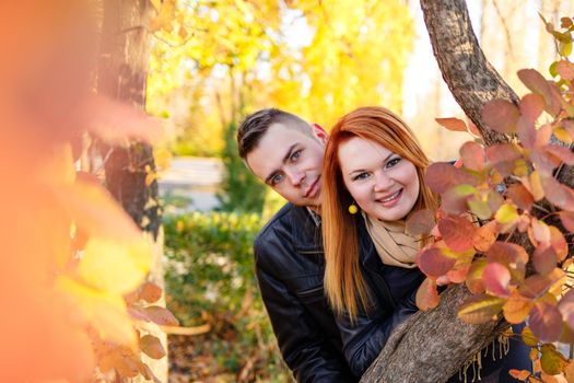 Young couple play hide and seek in the park in autumn day