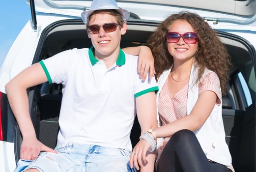 young couple sitting in the open trunk of a new car, a summer road trip