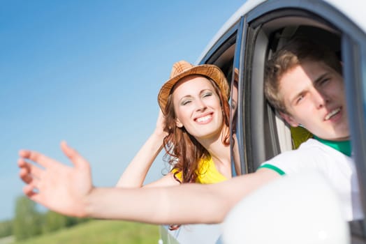 Young woman looking out of car window, holds the hand hat and smiling