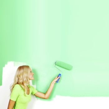 Smiling young woman painting the wall with roller brush