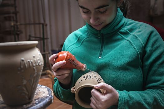 Potter decorating with enamel a ceramics piece before putting in the stove with branches drawings, clay pottery ceramics typical of Bailen, Jaen province, Andalucia, Spain