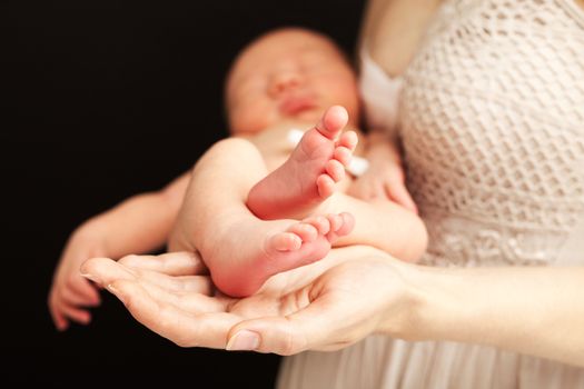 Young caucasian woman holding newborn son over black background