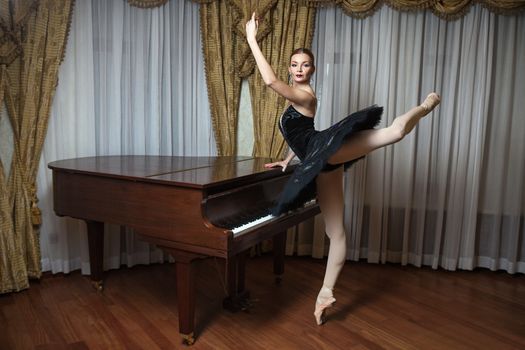Ballerina in black tutu standing on pointes at the grand piano