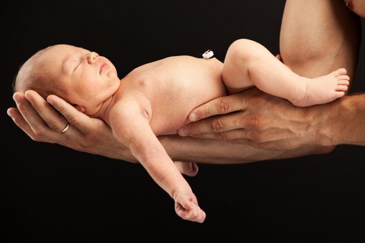 Newborn boy lying on his dad's arms over black background