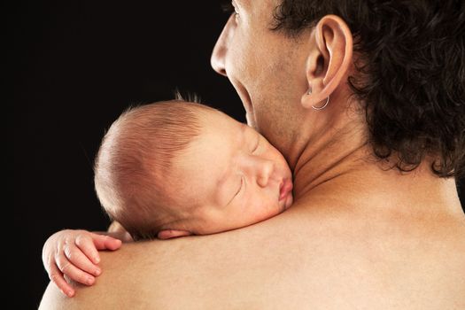 Newborn boy sleeping on his dad's shoulder over black background