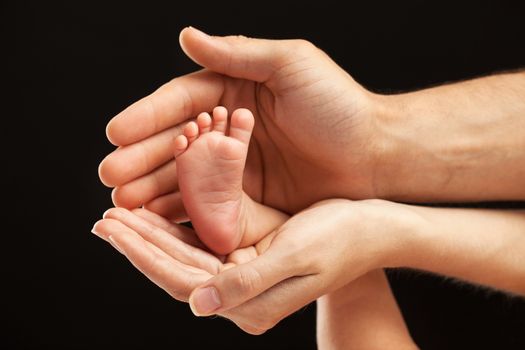 Newborn baby foot in parents hands over black background