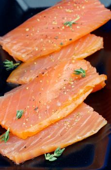 Slices of Delicious Smoked Salmon with Thyme closeup on Black Plate