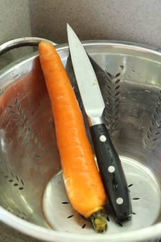 kitchen knife and carrot in a colander