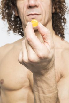 Cropped shot of bare chested mediterranean man holding colourful pill