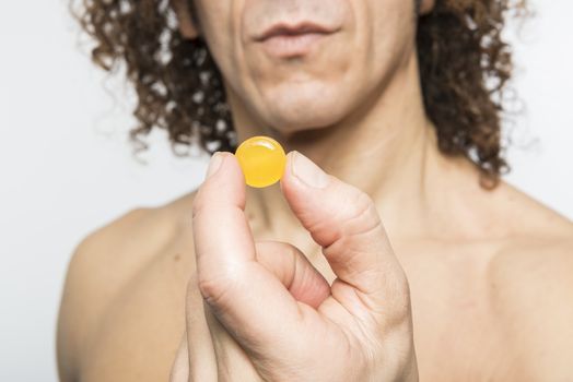 Cropped shot of bare chested mediterranean man holding colourful pill
