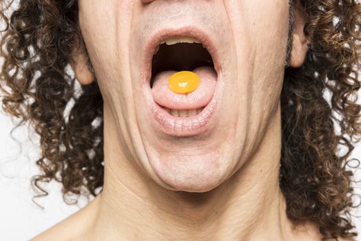 Cropped shot of mediterranean man with orange pill in his tongue