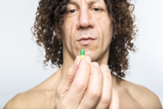 Cropped shot of bare chested mediterranean man holding colourful pill