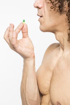 Cropped shot of bare chested mediterranean man taking colourful pill