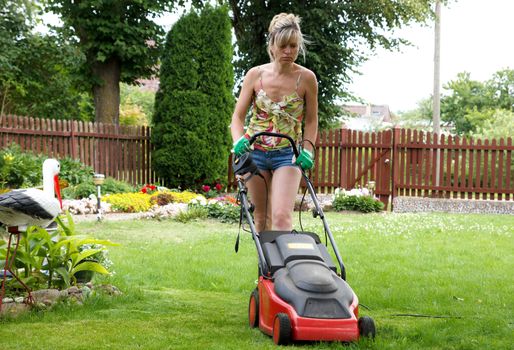 Woman cuts the grass with an electric lawn mower