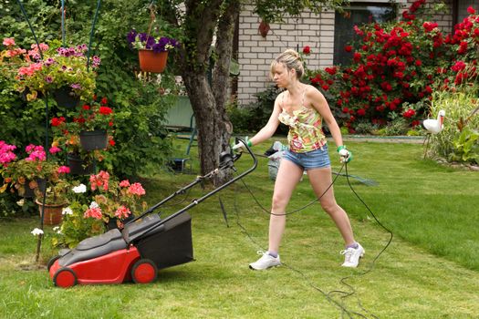 Woman cuts the grass with an electric lawn mower