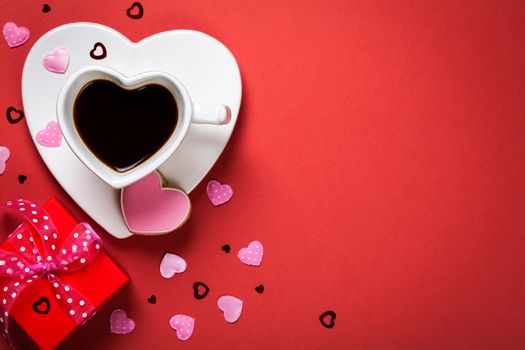 Coffee with red gift box and cookie in shape of heart. Composition for Valentines Day on red paper background. Top view. Copy space