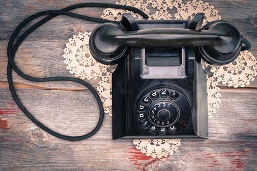 View from above of a black old-fashioned rotary telephone instrument on a crocheted doily on a weathered wooden table top