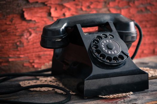 Close up side view of an old classic black dial-up rotary telephone against a grunge wooden wall with peeling red paint