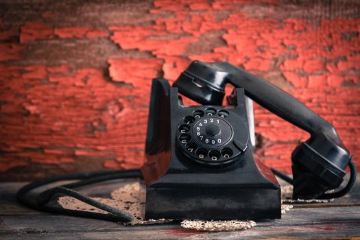 Old-fashioned rotary telephone with the handset off the hook effectively blocking the line against a rustic wall with distressed peeling red paint