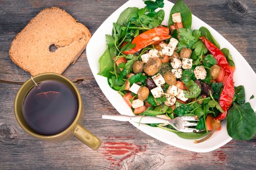 Overhead view of a dish of delicious fish leafy green baby spinach salad with bread and tea on a rustic wooden surface