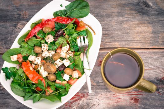 Bowl of fresh leafy green baby spinach and tomato salad with a freshly brewed mug of hot tea on a rustic wooden table, overhead view