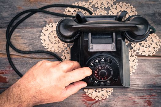 Man making a call on a rotary telephone dialing the numbers with his finger , high angle view of the instrument on an old wooden surface