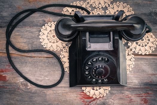 High angle closeup view of an old black rotary phone on a decorative criocheted doily with the handset on the cradle