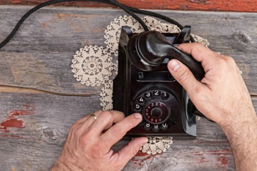 High angle view of the hands of a married man dialing out on an old rotary telephone standing on a weathered rustic table top