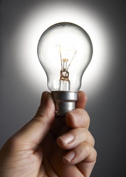 Mans hand holding a light bulb against grey background