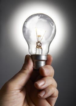 Mans hand holding a light bulb against grey background