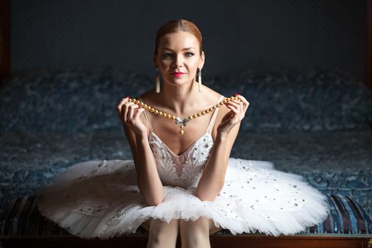 Ballerina sitting on bed holding pearl necklace