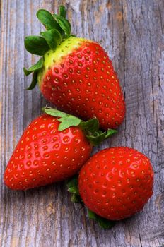 Three Ripe Strawberries with Stems closeup on Rustic Wooden background