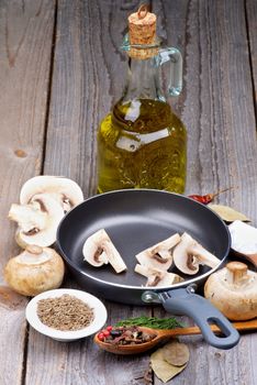 Preparing to Roast Edible Mushrooms in Frying Pan  with Spices, Olive Oil and Greens closeup on Rustic Wooden background