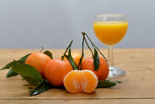 several mandarins with a glass of juice on the wooden table