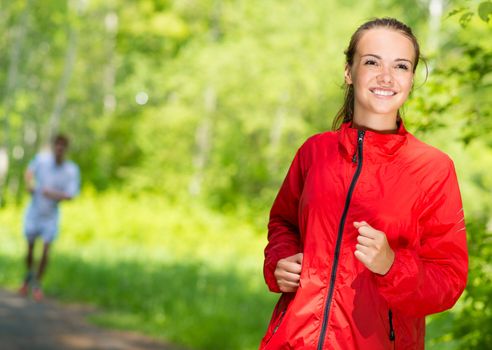 healthy young female athlete running in a summer park smiling and happy while working out