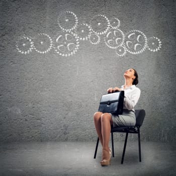 image of a beautiful young business woman sitting on a chair and looking at the gears on