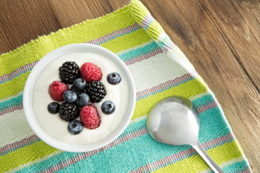 Delicious yogurt and fresh berries for breakfast with strawberries, blackberries and blueberries served on a colourful striped placemat