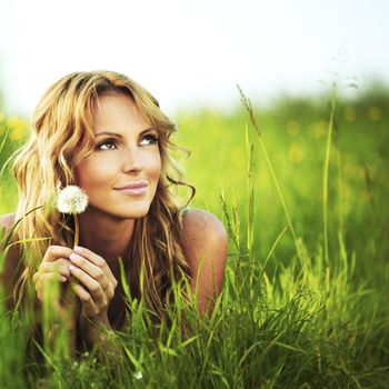 Young woman with dandelion lying on grass