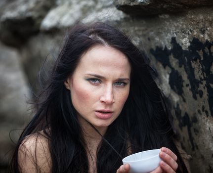 Young cute girl in a knitted sweater against a background of an old concrete wall drinking tea from a white cup
