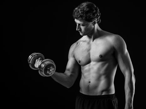 Photo of a man in his early thirties doing bicep curls with a dumbbell over a black background. Black and white version.