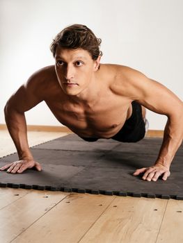 Photo of a man in his early thirties doing pushups on a mat in a fitness centre.
