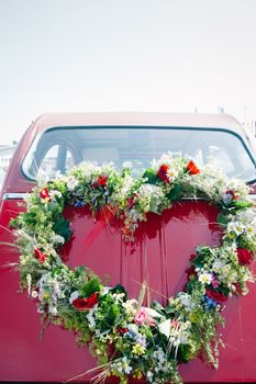 Heart shape bouquet on the rear end of a red wedding car