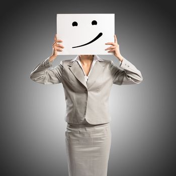 business woman holding a poster with a painted face on it instead of a face, the concept of duplicity in business